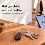 AirTag-Halter an einem Schlüsselbund auf dem Tisch, mit Smartphone im Hintergrund
