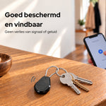 AirTag-houder aan een sleutelbos op tafel, met een telefoon op de achtergrond